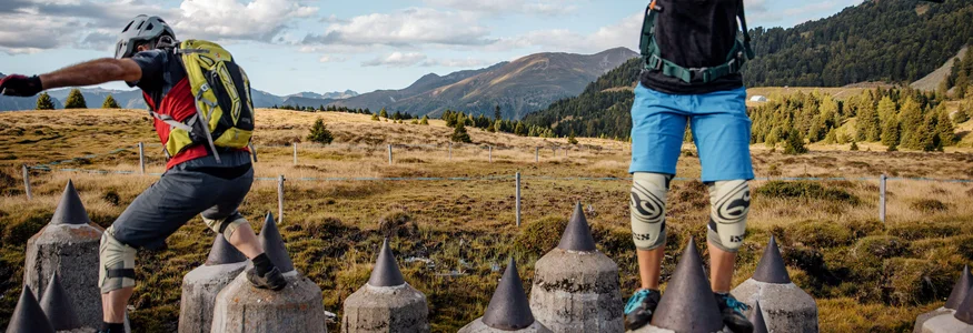 Zwei Personen balancieren auf spitzen Betonpfeilern in bergiger Landschaft