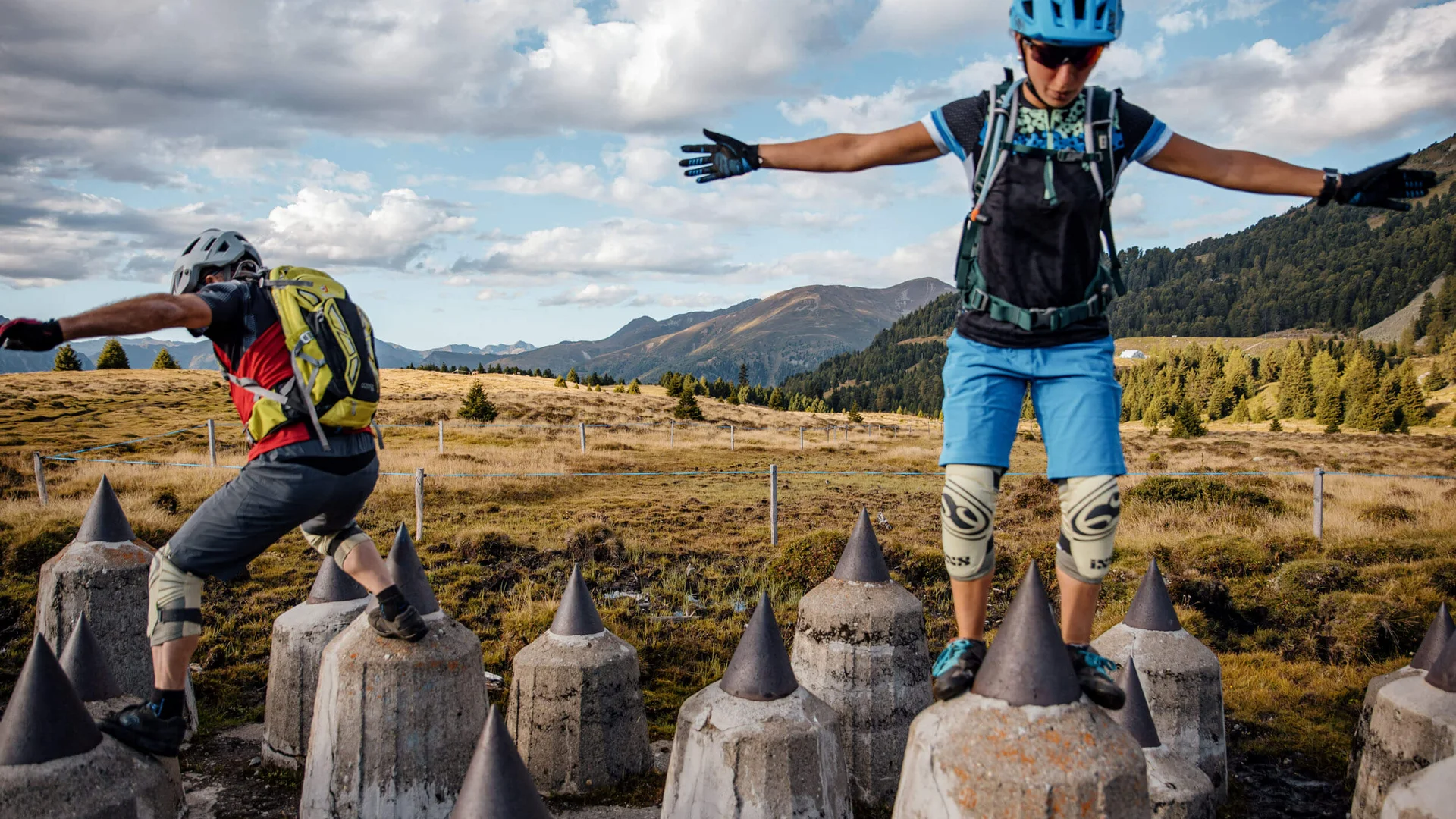 Two people balancing on pointed concrete pillars in mountainous area
