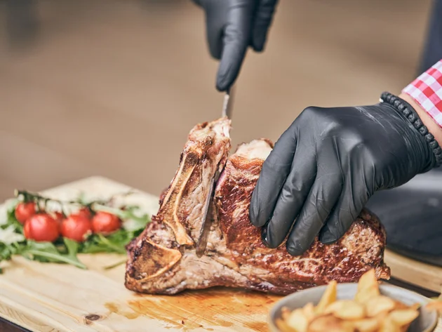 Persoon snijdt gebakken biefstuk met zwarte handschoenen