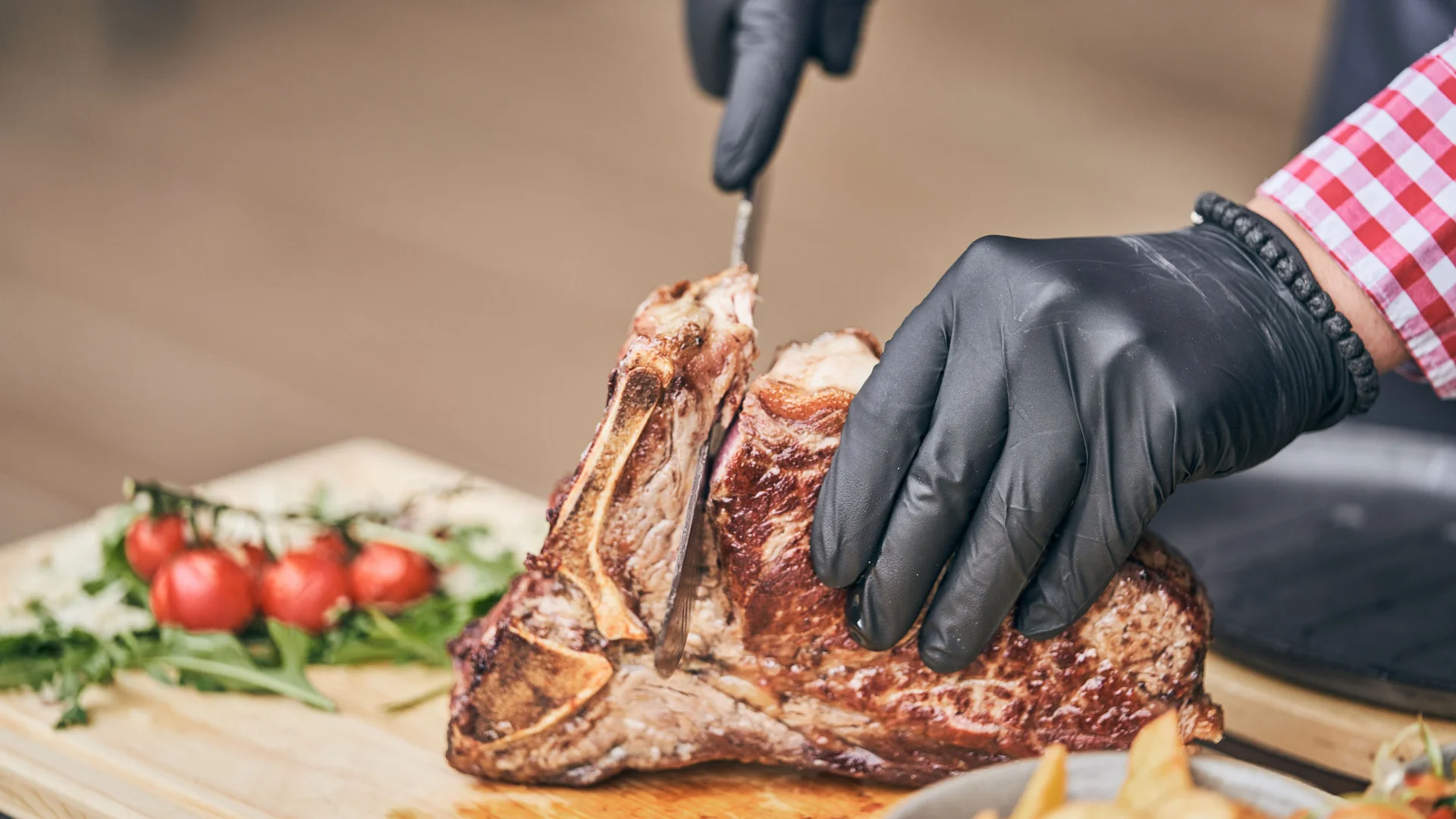 Person schneidet gebratenes Steak mit schwarzer Handschuh