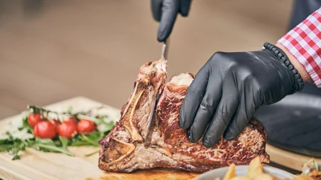 Persoon snijdt gebakken biefstuk met zwarte handschoenen