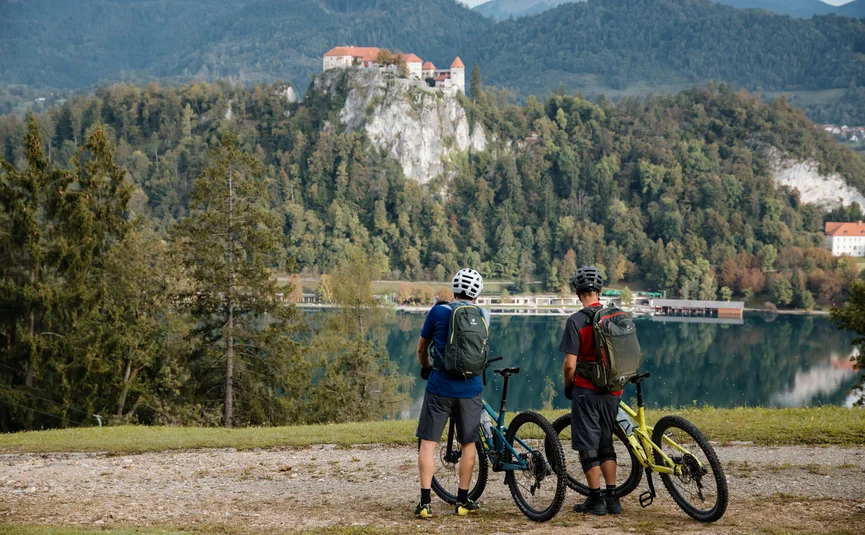 Zwei Radfahrer mit Helm schauen auf ein Schloss auf einem Hügel am See
