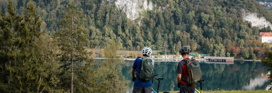 Zwei Radfahrer mit Helm schauen auf ein Schloss auf einem Hügel am See
