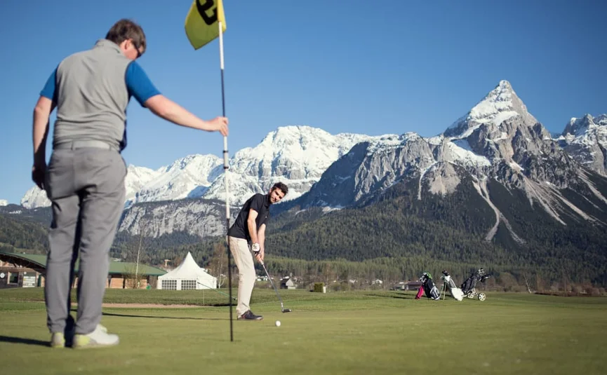 Two men playing golf with snowy mountains in the background.