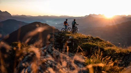 Zwei Mountainbiker stehen auf Berggipfel bei Sonnenuntergang