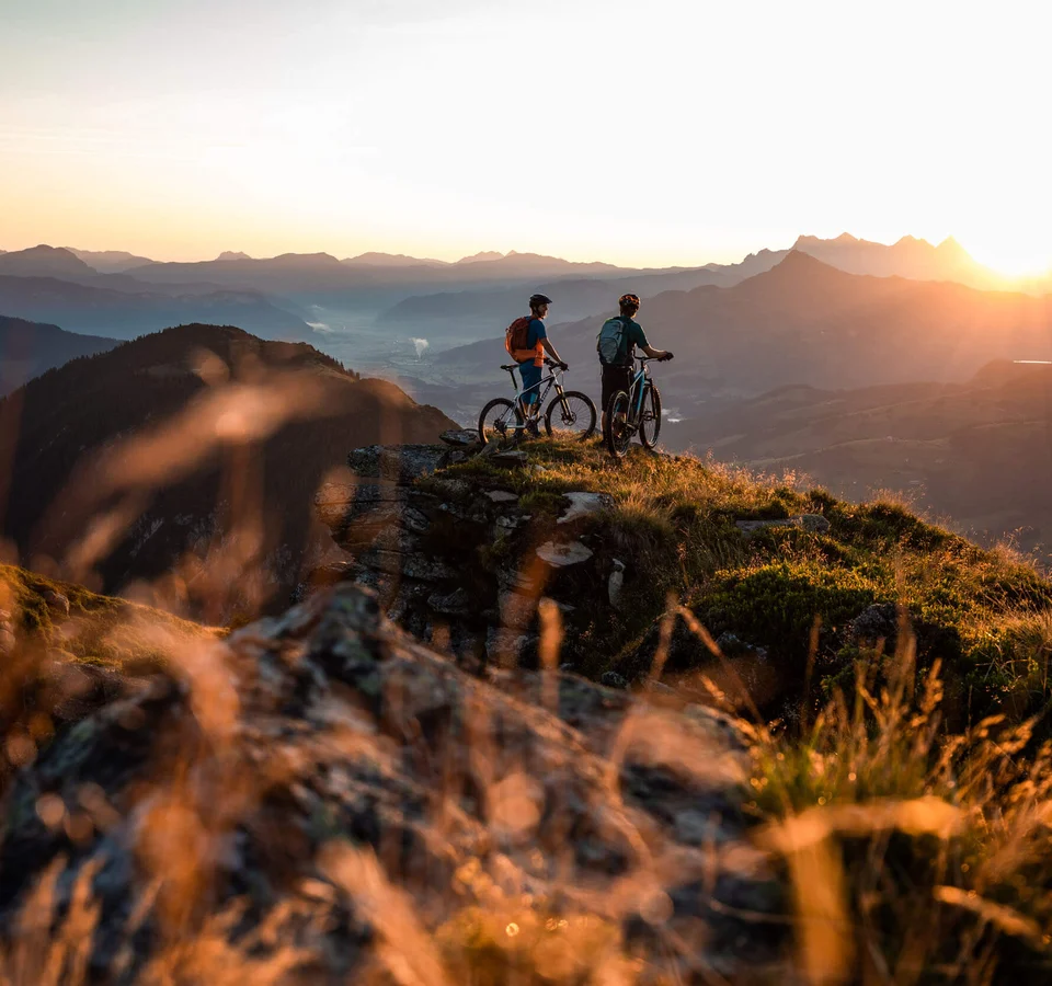 Zwei Mountainbiker stehen auf Berggipfel bei Sonnenuntergang