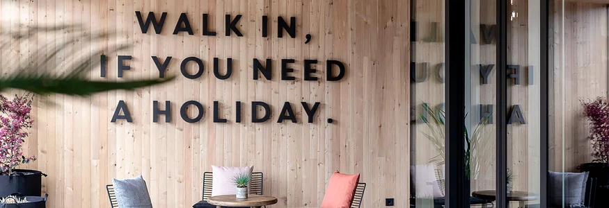 Sitzbereich mit Stühlen, Tisch und Wandtext Walk in, if you need a holiday