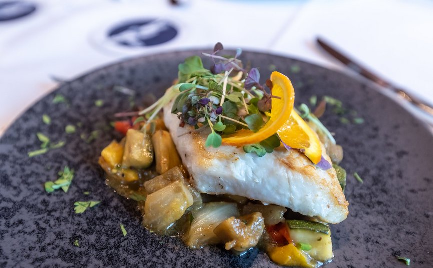 Gebratenes Fischfilet mit Gemüse und Orangenscheibe auf dunklem Teller