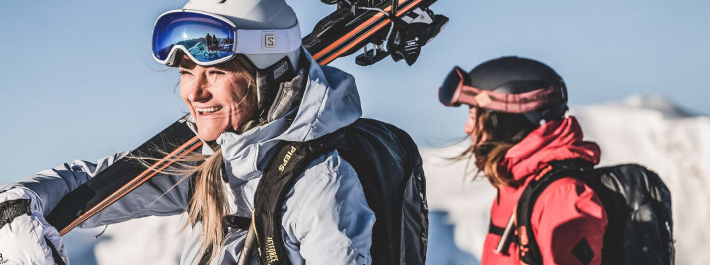 Zwei Skifahrer in Winterkleidung mit Ausrüstung vor verschneiten Bergen