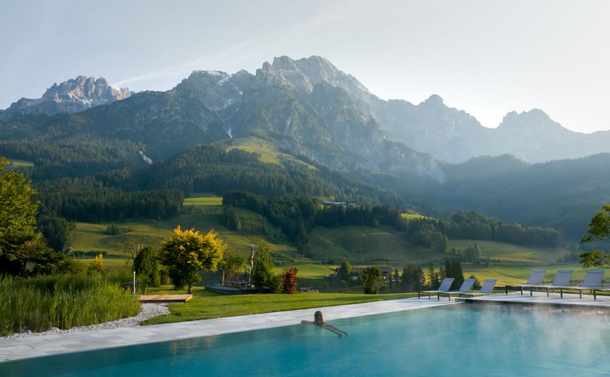 Puradies © creatingclick Person entspannt im Pool mit Blick auf bewaldete Berge und grüne Wiesen