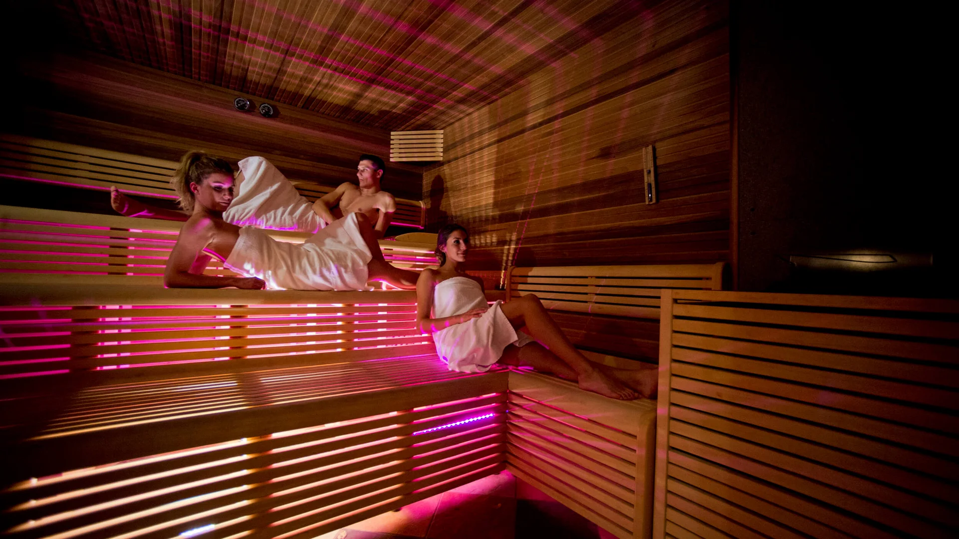 Good to know: 9 Wellness-Funfacts © Fabio Staropoli Drei Personen entspannen in einer Sauna mit Holzwänden und rosa Licht