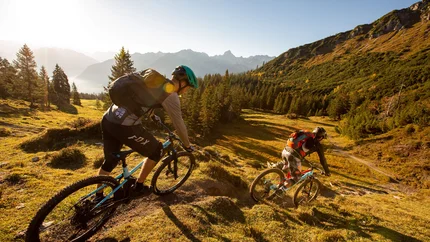 Zwei Mountainbiker fahren bergab in einer sonnigen Berglandschaft