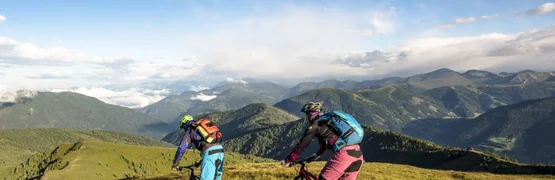 Zwei Mountainbiker fahren auf einem Bergweg mit Alpenpanorama