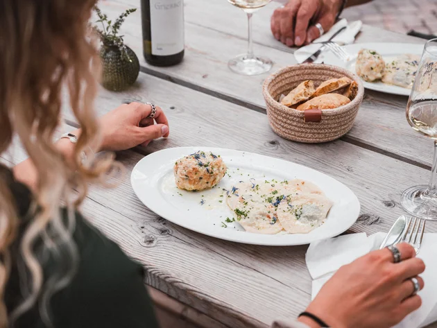 Mountainbiken im Herbst: 5 Top-Regionen für die Saisonverlängerung © Brixen Tourismus - Hannes Engl Person isst Nudeln und Knödel mit Wein auf Holztisch