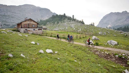 Cyclists on a path near a mountain cabin in the Alps
