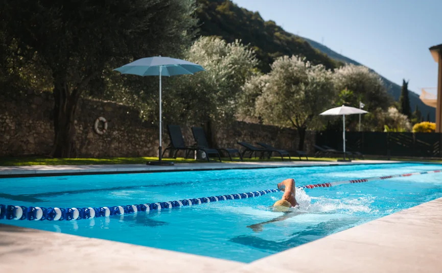 Swimmer in outdoor pool with umbrellas and trees in the background