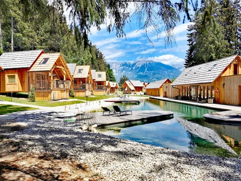 Hotel & Glamping Ribno Alpine Resort © Ribno Alpine Resort - Katarina Strgar Holzhütten am See mit Bergblick und zwei Liegestühlen am Steg
