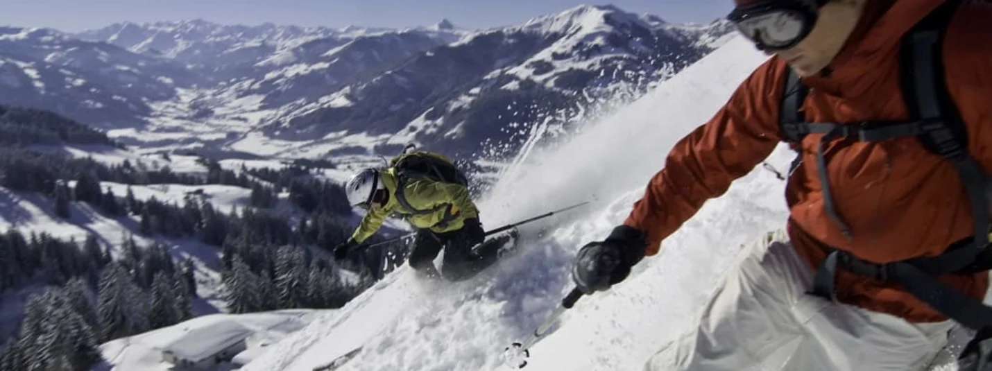 Schnee(s)pass 1-4+3 Twee skiërs dalen af door diepe sneeuw met besneeuwde bergen op de achtergrond