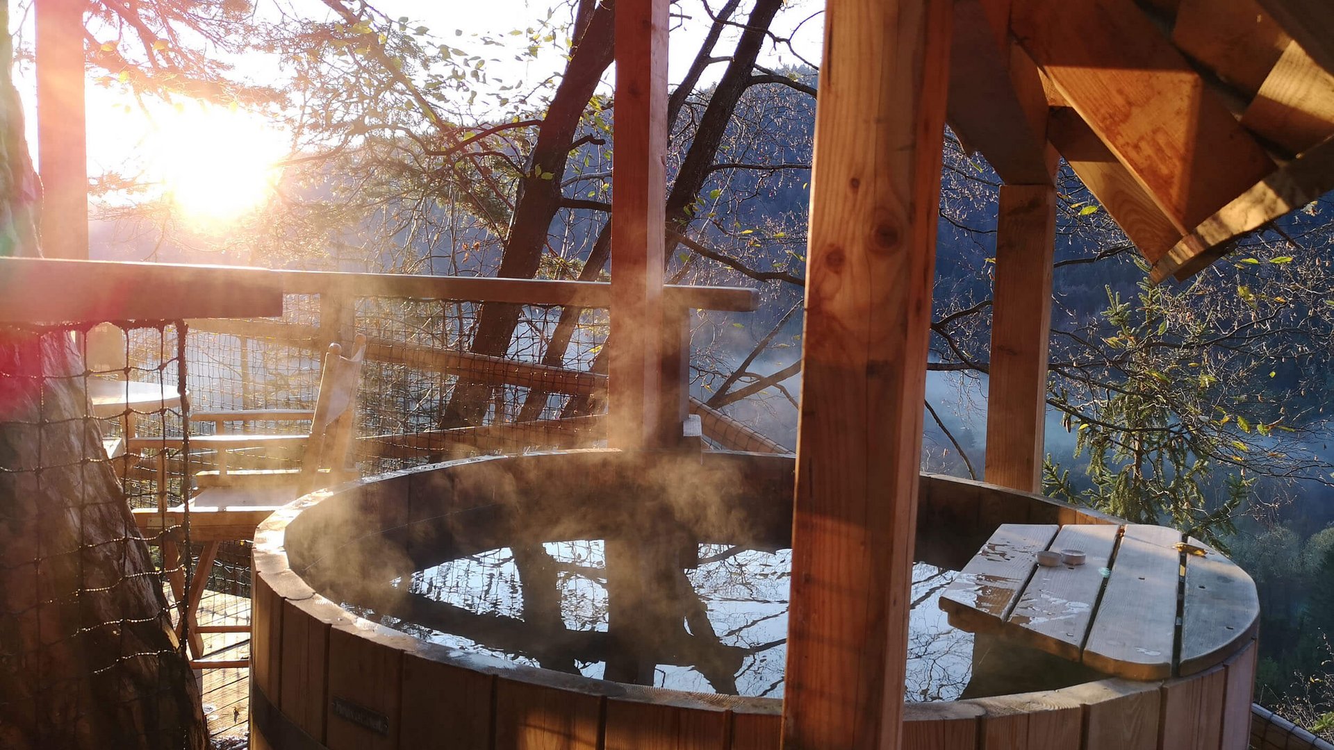 Dampfende Holzbadewanne auf altem Balkon bei Sonnenuntergang
