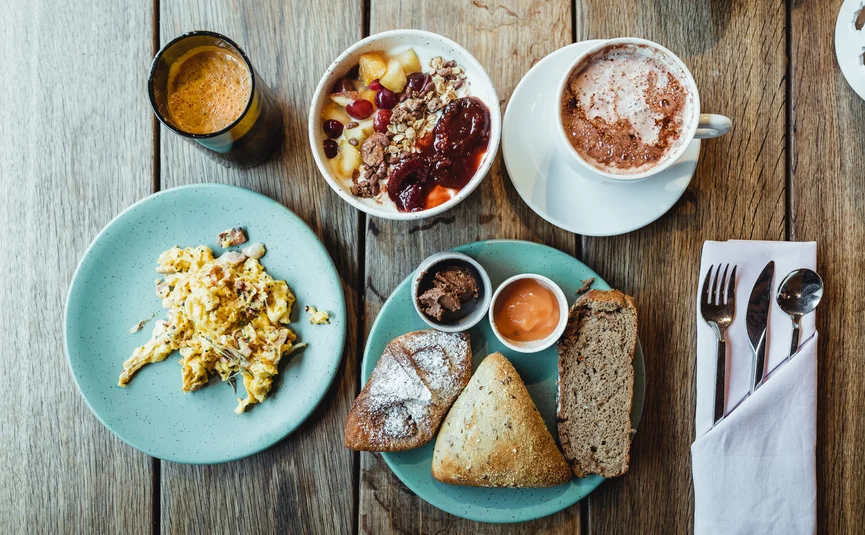 Frühstück mit Rührei, Brot, Müsli, Kaffee und Orangensaft auf Holztisch