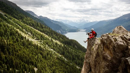 Mann sitzt auf Felsen mit Berg- und Seeblick