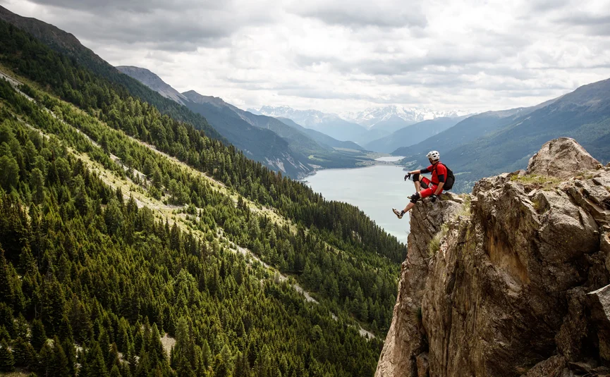 Mann sitzt auf Felsen mit Berg- und Seeblick