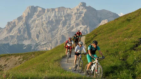 Mountainbike-Urlaub in Alta Badia © Hotel Melodia del Bosco Fünf Radfahrer fahren auf Bergweg mit großem Felsgebirge im Hintergrund