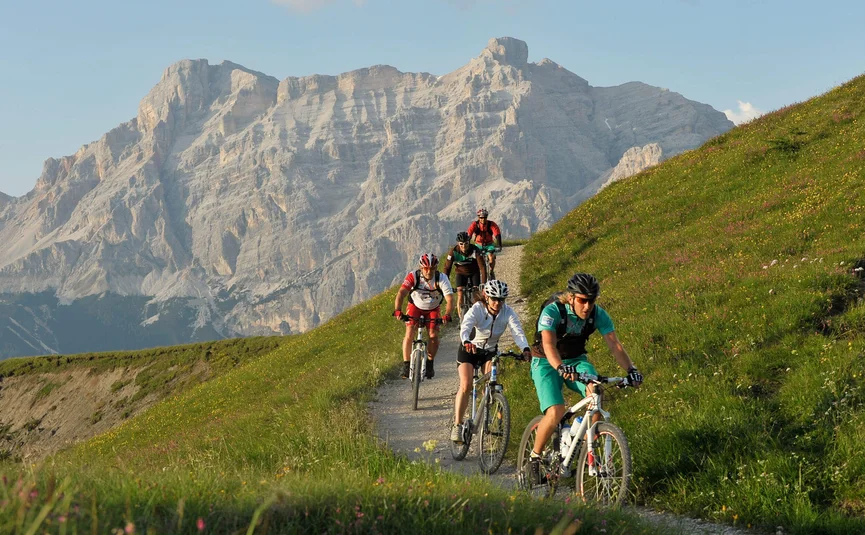 Fünf Radfahrer fahren auf Bergweg mit großem Felsgebirge im Hintergrund