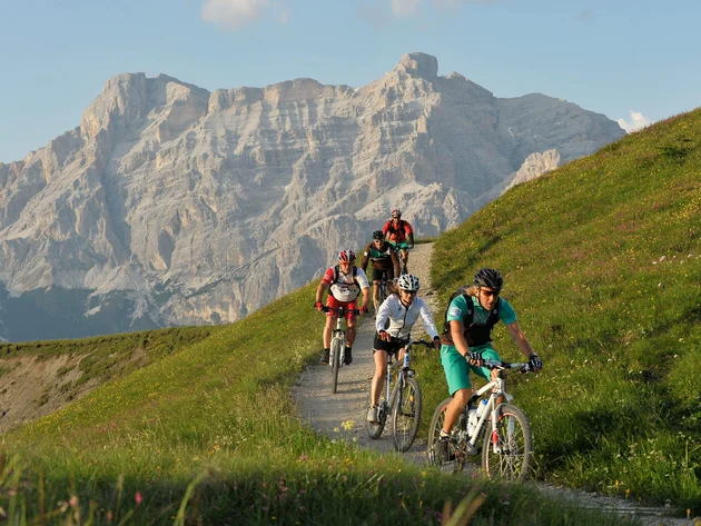 Mountainbike-Urlaub in Alta Badia © Hotel Melodia del Bosco Fünf Radfahrer fahren auf Bergweg mit großem Felsgebirge im Hintergrund
