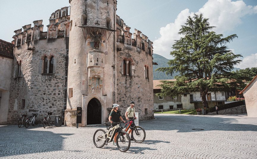 Mountain bike holiday in Brixen © Brixen Tourismus - Hannes Engl Two cyclists in front of a historic stone tower on a sunny day