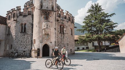 Zwei Radfahrer vor einem historischen steinernen Turm an einem sonnigen Tag
