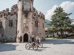 Zwei Radfahrer vor einem historischen steinernen Turm an einem sonnigen Tag