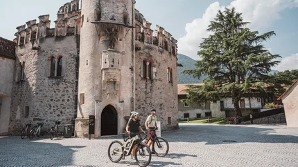 Twee fietsers voor een historische stenen toren op een zonnige dag