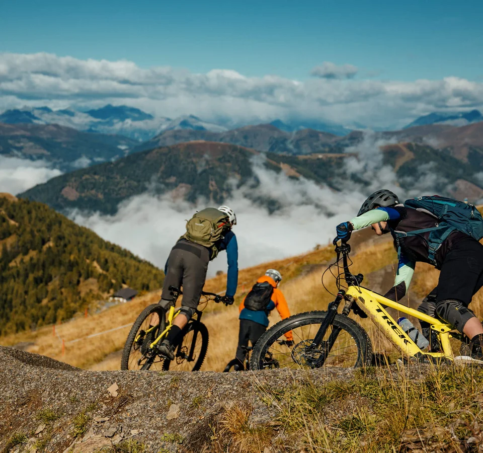Drei Mountainbiker fahren auf einem Pfad in den Bergen bei klarem Himmel