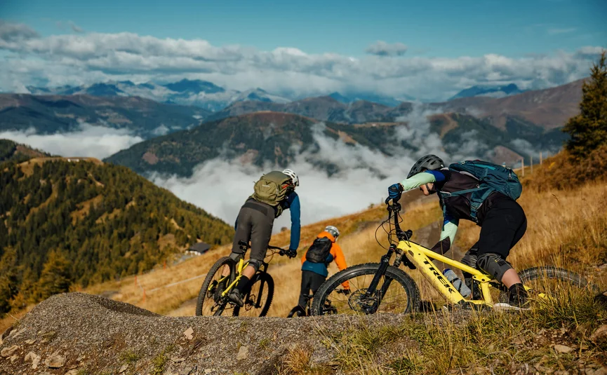 Drei Mountainbiker fahren auf einem Pfad in den Bergen bei klarem Himmel