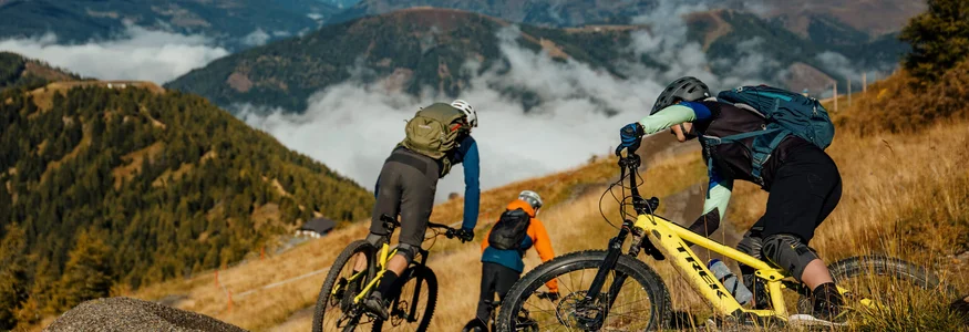 Drei Mountainbiker fahren auf einem Pfad in den Bergen bei klarem Himmel