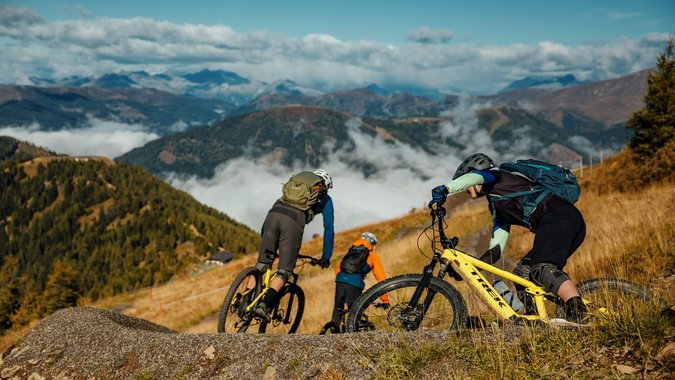 Drei Mountainbiker fahren auf einem Pfad in den Bergen bei klarem Himmel