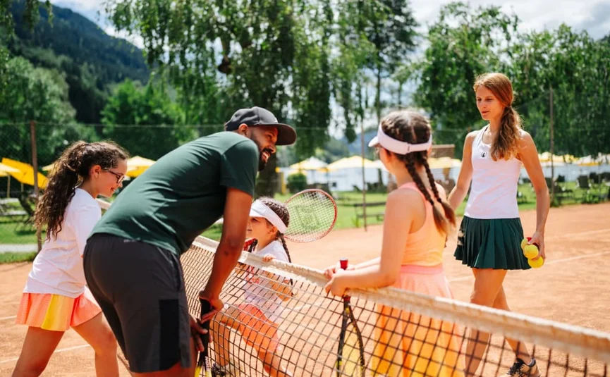 Tennistrainer unterhält sich mit drei Mädchen auf Sandplatz im Freien