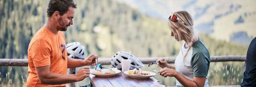 Zwei Personen essen draußen mit Berglandschaft im Hintergrund