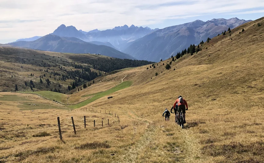 Three mountain bikers riding on a trail through hilly alpine landscape