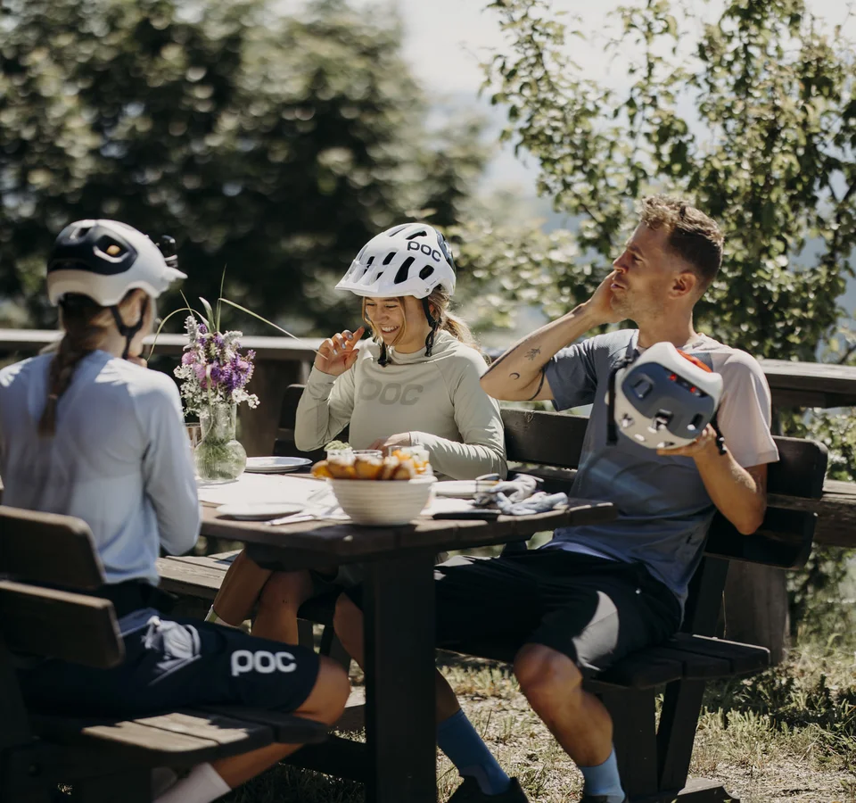 Bye bye Tauernhof, hello Dips&Drops! Fahrradfahrer in Helmen sitzen draußen an einem Holztisch und lachen