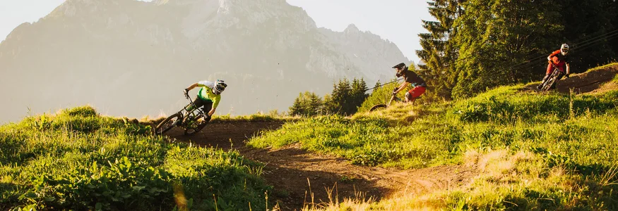 Drei Mountainbiker fahren auf einem Bergtrail bei sonnigem Wetter