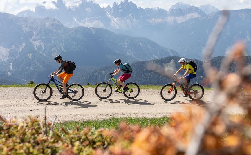 Drei Radfahrer fahren auf Bergweg mit Alpen im Hintergrund
