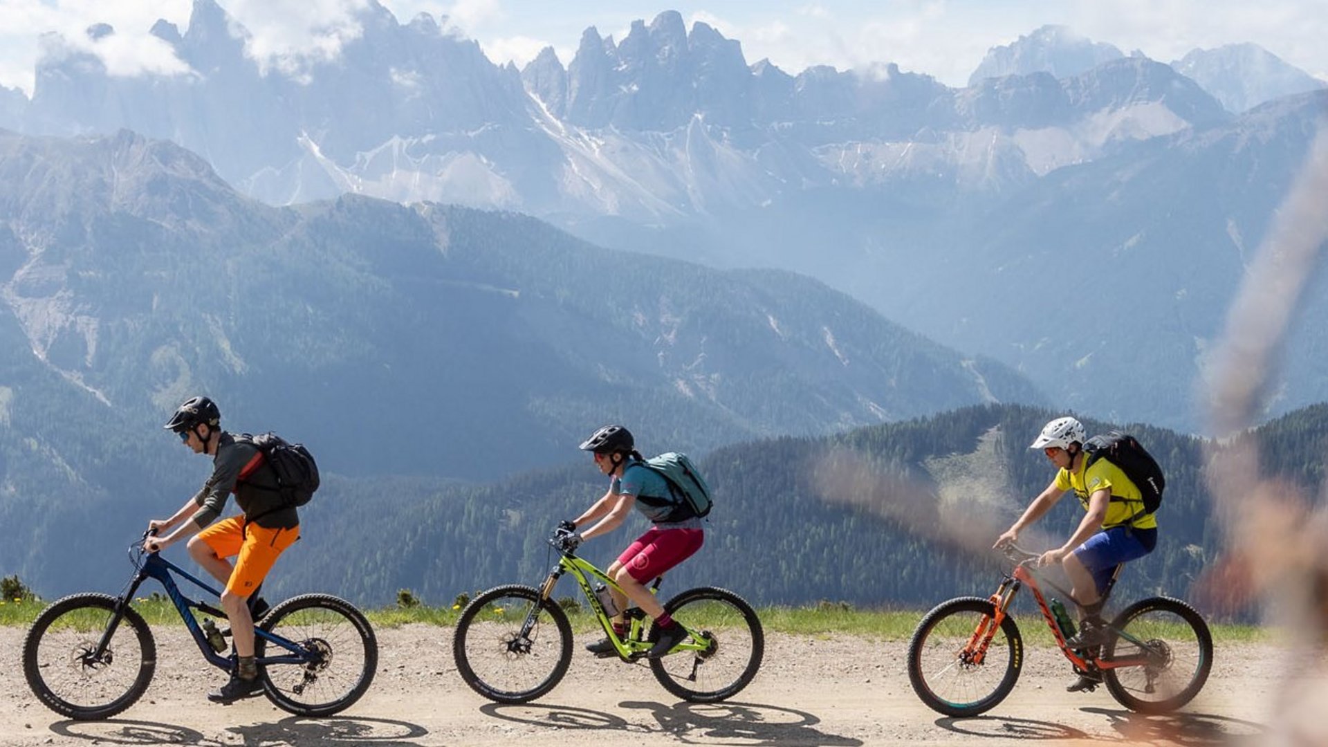 Drei Radfahrer fahren auf Bergweg mit Alpen im Hintergrund