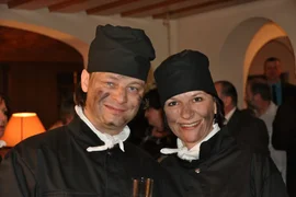 Ski, Gourmet & Dorfsilvester Twee lachende mensen in zwarte kokskleding en koksmutsen tijdens een bijeenkomst