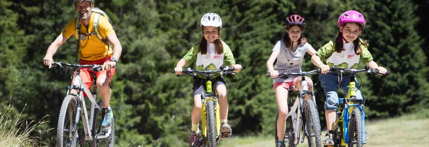 Vater und drei Kinder fahren mit Fahrrädern auf einem Waldweg