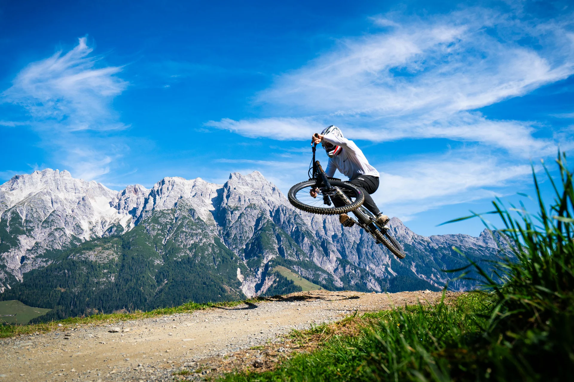 Mountainbiker macht einen Sprung auf einem Bergweg mit Alpen im Hintergrund