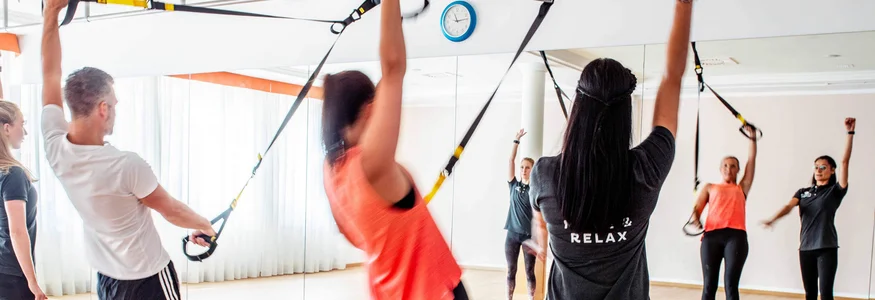 Gruppe von Menschen beim TRX-Training in einem Fitnessstudio mit Spiegel
