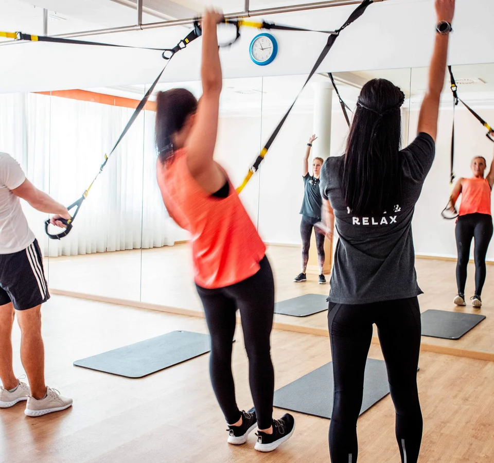 Gruppe von Menschen beim TRX-Training in einem Fitnessstudio mit Spiegel