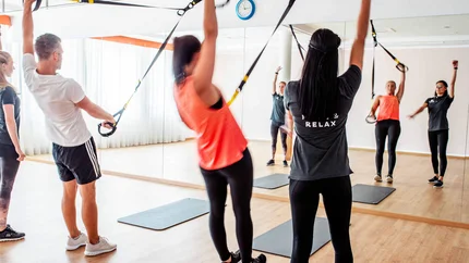 Gruppe von Menschen beim TRX-Training in einem Fitnessstudio mit Spiegel
